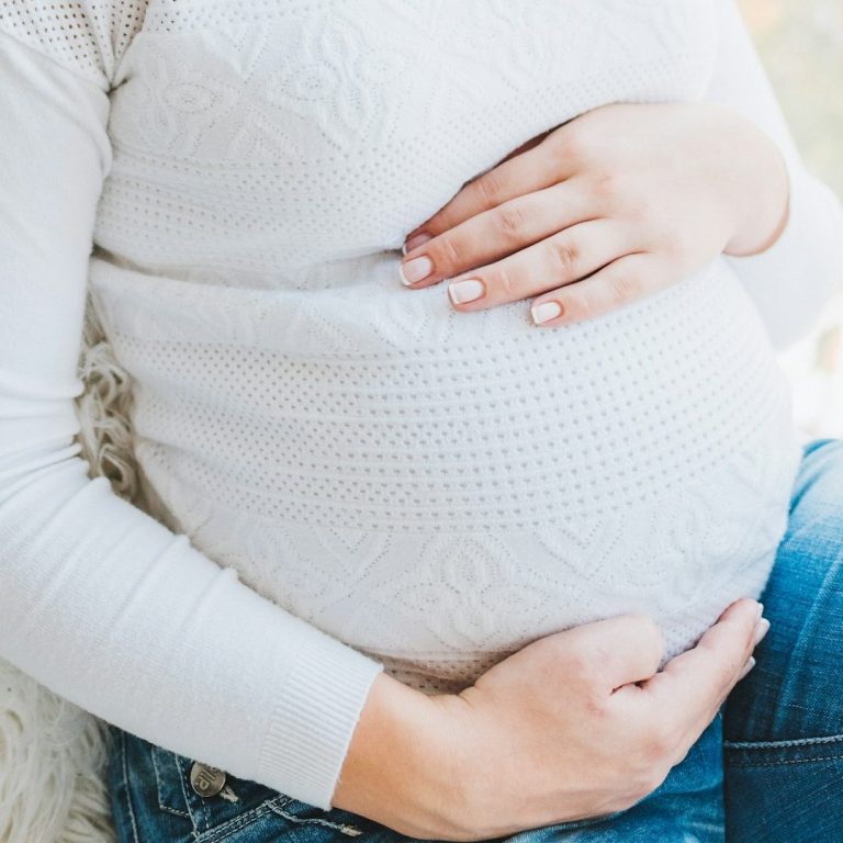 Schwangere Person mit Händen auf dem Bauch,